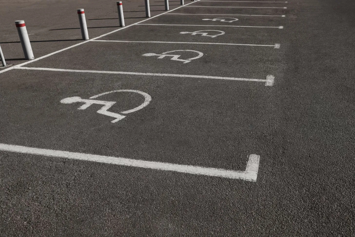 Photo of a row of four accessible parking spaces, marked on black pavemenet with white lines and wheelchair symbols
