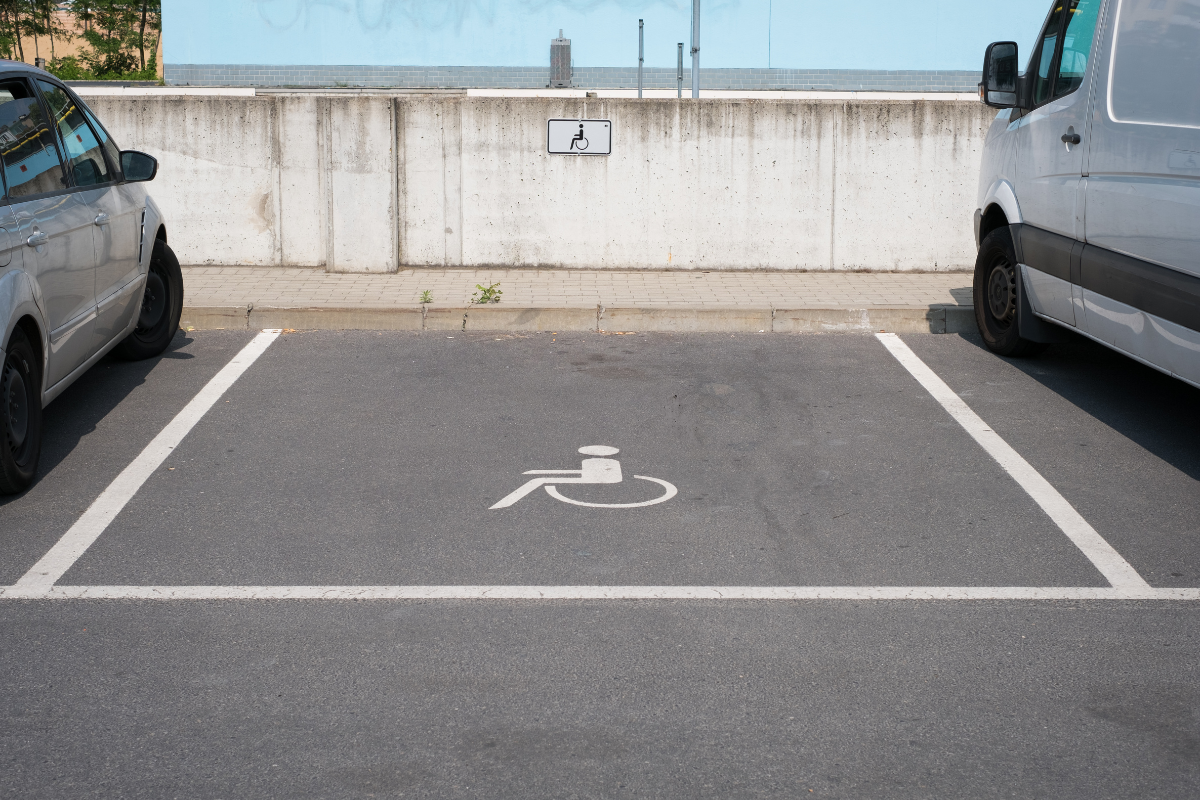 Accessible parking space marked by wheelchair symbols on pavement and wall, with cars parked on either side
