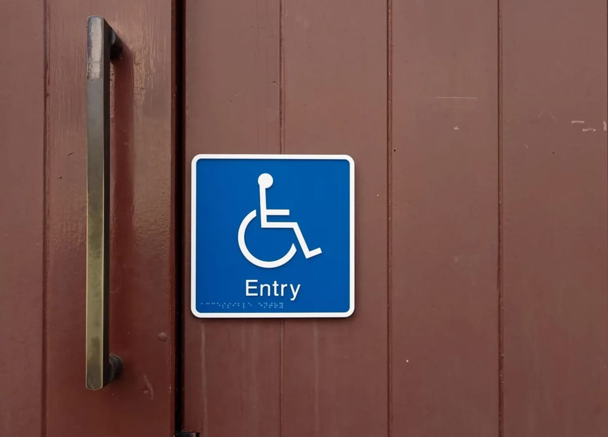 White on blue wheelchair symbol sign labeled "entry" mounted on a wooden door