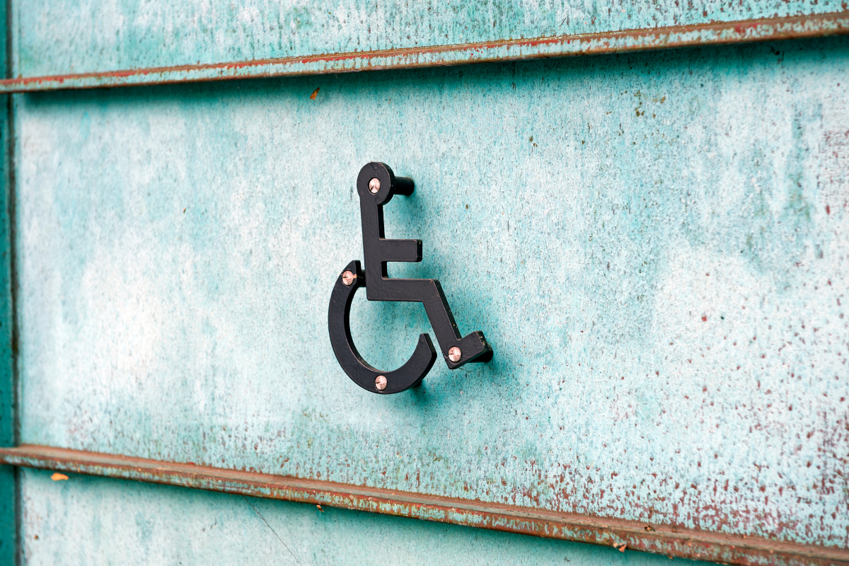 Metal sculpture of a wheelchair symbol riveted onto a cement wall