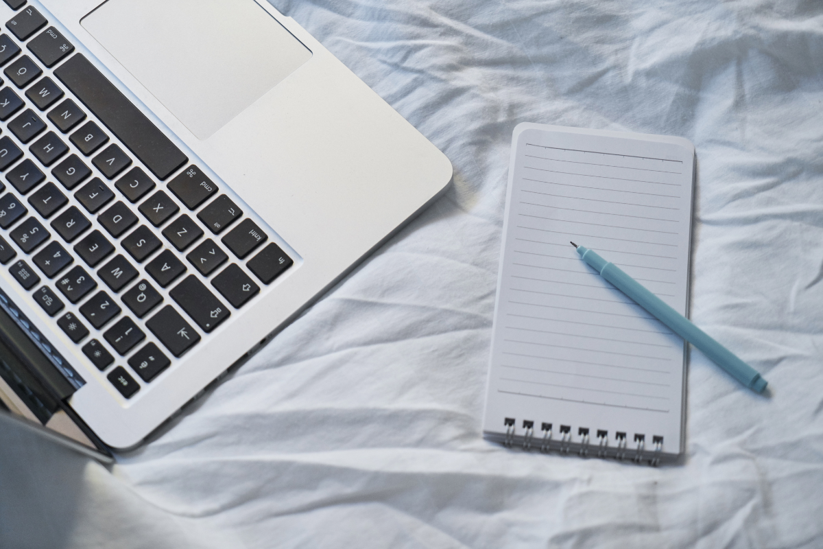 Laptop computer keyboard, note pad, and pen viewed from above on a fabric covered table