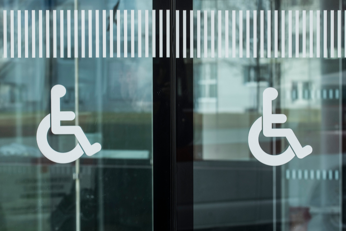 Two white wheelchair symbol decals on tinted glass doors