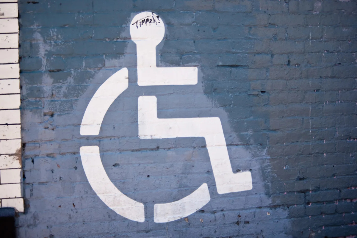 White wheelchair symbol stenciled on a blue painted brick wa