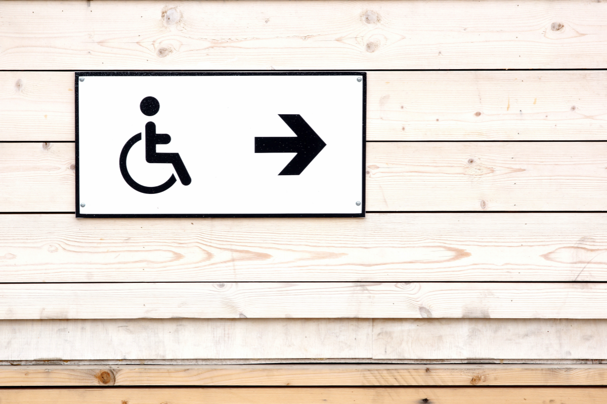 Wheelchair symbol and arrow pointing right on a sign mounted on a wooden wall