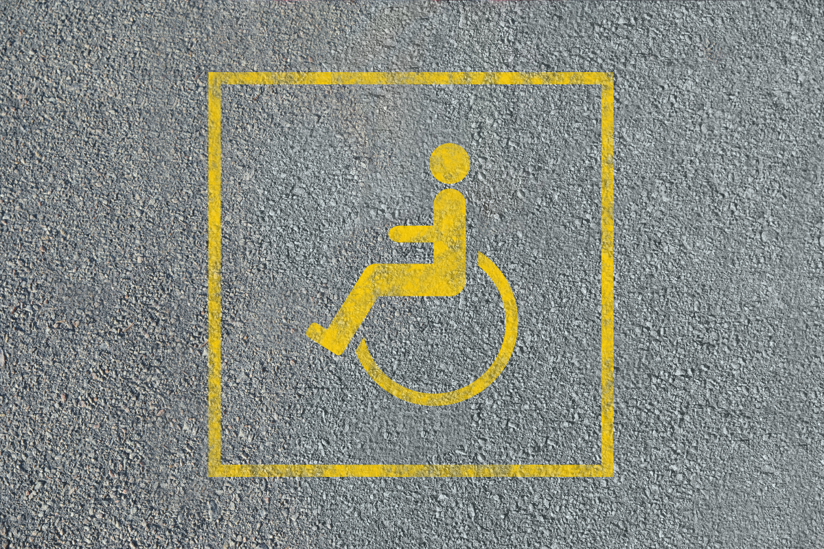 Wheelchair symbol in a quart, painted in faded yellow paint on grey tarma