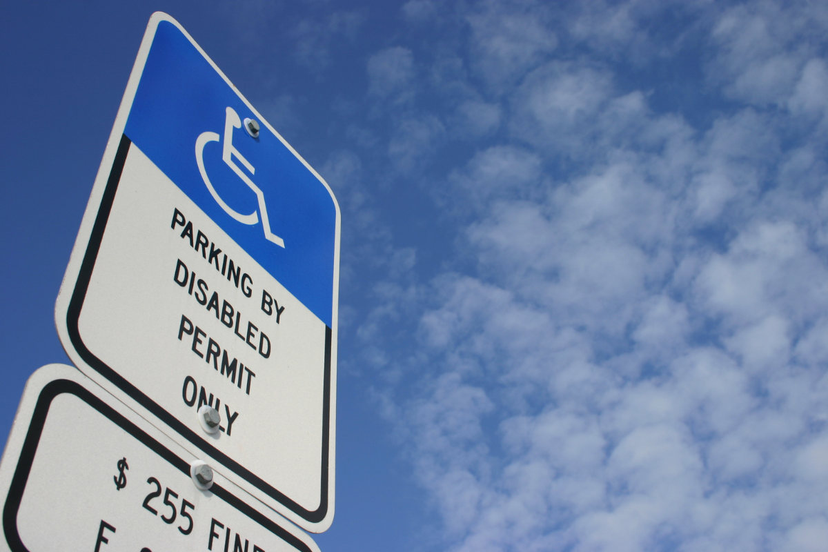 "PARKING BY DISABLED PERMIT ONLY" sign viewed from a low angle against a partly cloudy sky