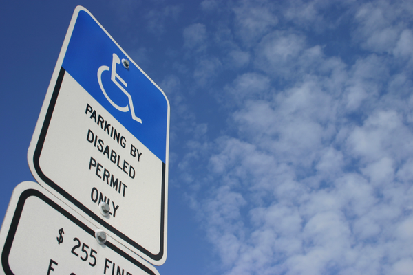 Sign marking accessible parking space viewed from below with lightly cloudy blue sky in backgroun