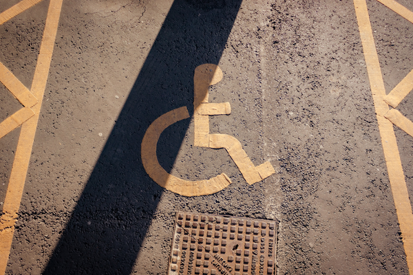 Yellow lines and wheelchair symbol marking accessible parking space on the pavement, with a shadow falling across it