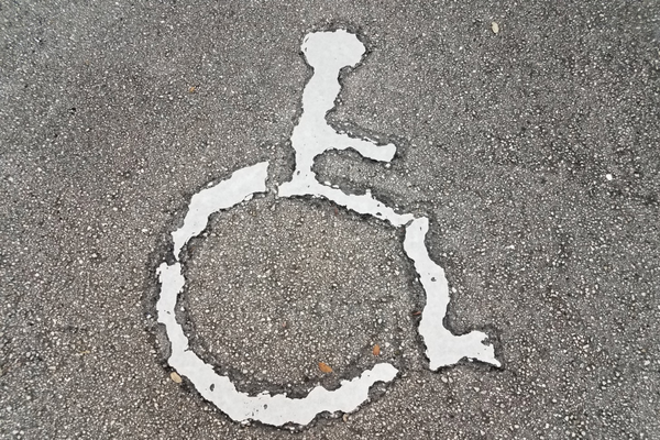 Wheelchair symbol, looking ragged and eroded, stenciled onto paveme