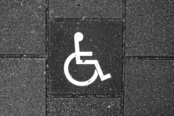 White wheelchair symbol stenciled on a wall of dark grey brick
