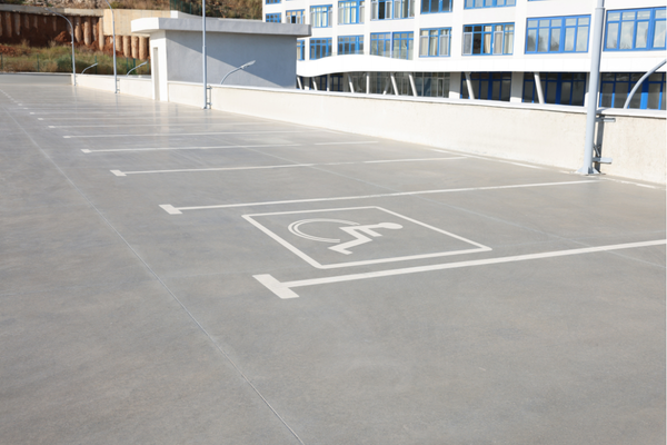 Wide angle view of a row of parking spaces in front of a building, the nearest one marked as accessible with a wheelchair symbol