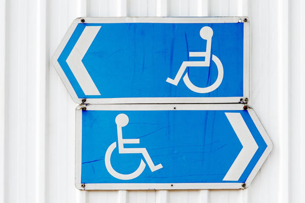 Two white on blue wheelchair symbol signs pointing in opposite directions on a white wall