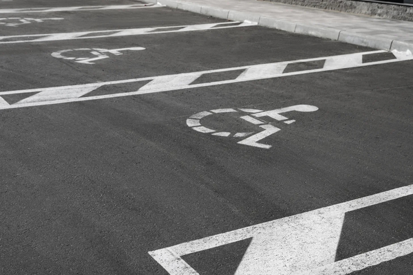 Black and white photo of a row of accessible parking spaces with wheelchair symbols and lanes stenciled on black pavement