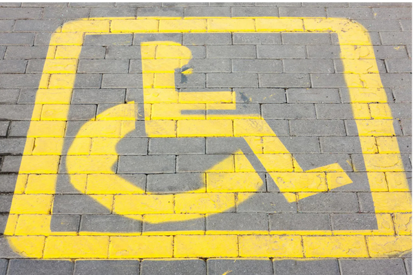 Yellow wheelchair symbol painted on grey brick pavement