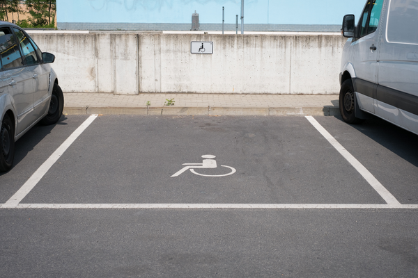Accessible parking space marked by wheelchair symbols on pavement and wall, with cars parked on either side