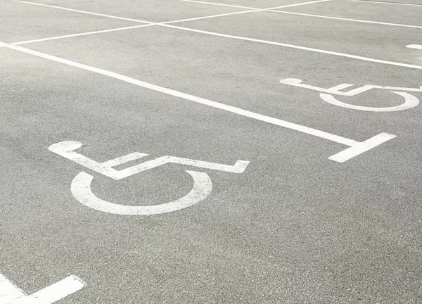 White wheelchair symbols pained on light gray pavement, marking accessible parking spaces