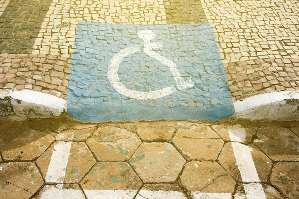White on blue wheelchair symbol roughly painted onto a cobblestone curb ramp