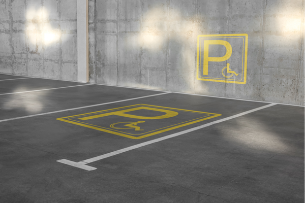 Sideways view of an accessible parking space with yellow symbols on grey pavement