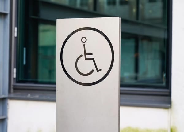 Black on light gray metal wheelchair sign outside a building