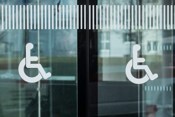2 white wheelchair symbols on blue green tinted glass doors