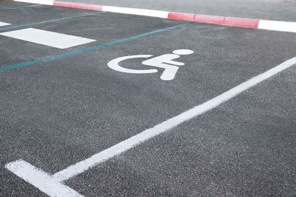 Stenciled white wheelchair symbol and lines marking accessible parking space on pavement