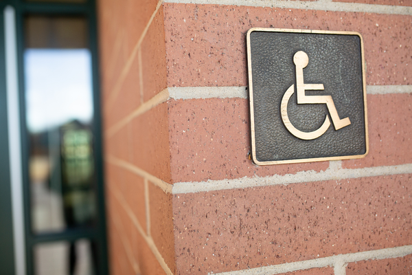Copper colored wheelchair symbol in a metal plaque mounted on an outdoor brick wall