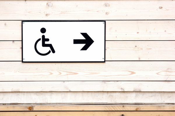 Black wheelchair symbol with a right-pointing arrow sign mounted on a wood paneled wall